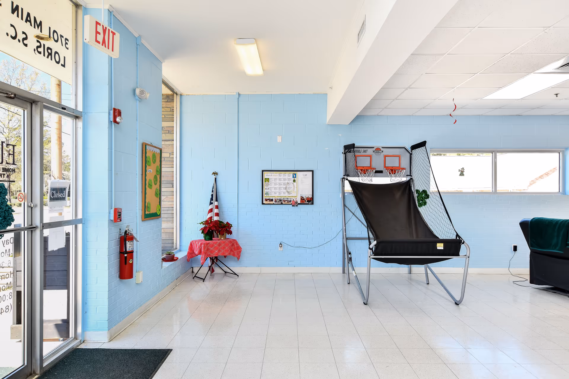 Entrance lobby with blue walls, exit sign, glass doors, and arcade basketball game.