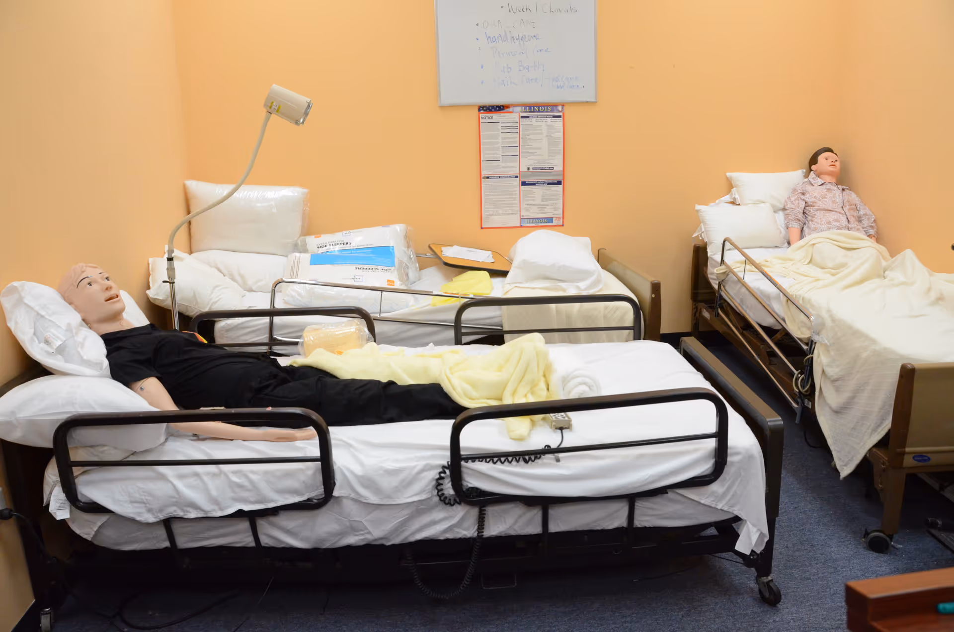 Two hospital beds with life-sized mannequins lie in a bright training room.