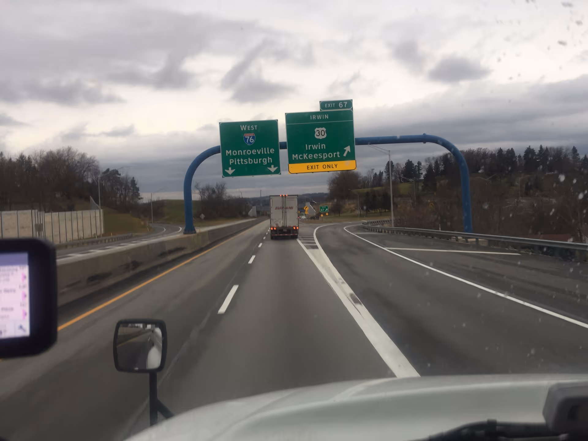 From a vehicle, highway view with overhead green exit signs and a truck ahead