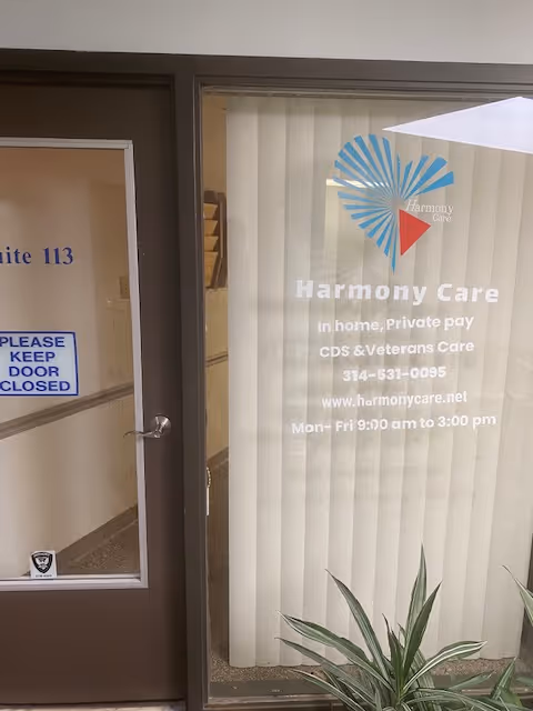 Glass entrance door with Harmony Care signage, vertical blinds, and a small plant nearby.