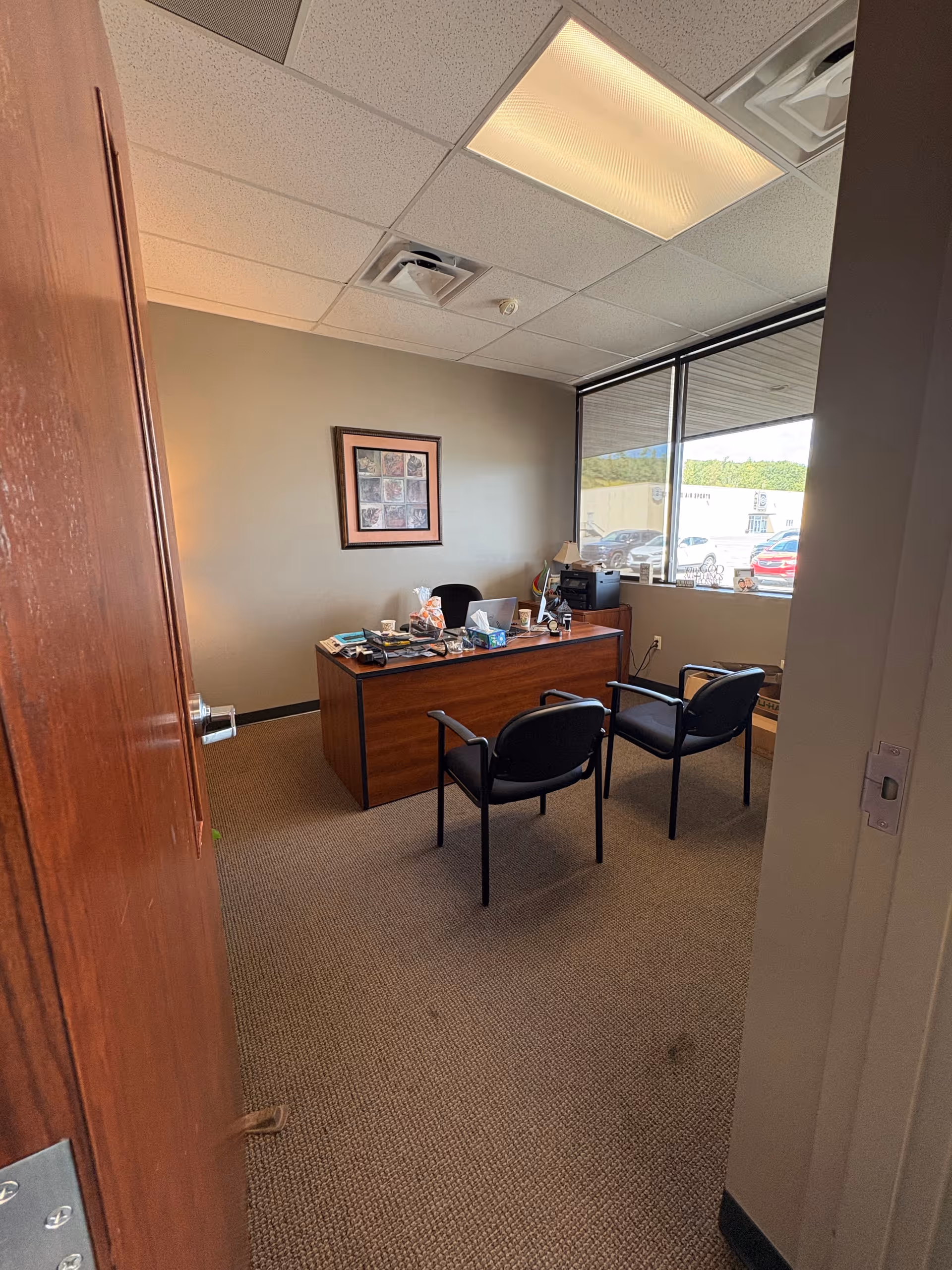 Office with desk, chairs, framed art, and a window overlooking the parking lot.