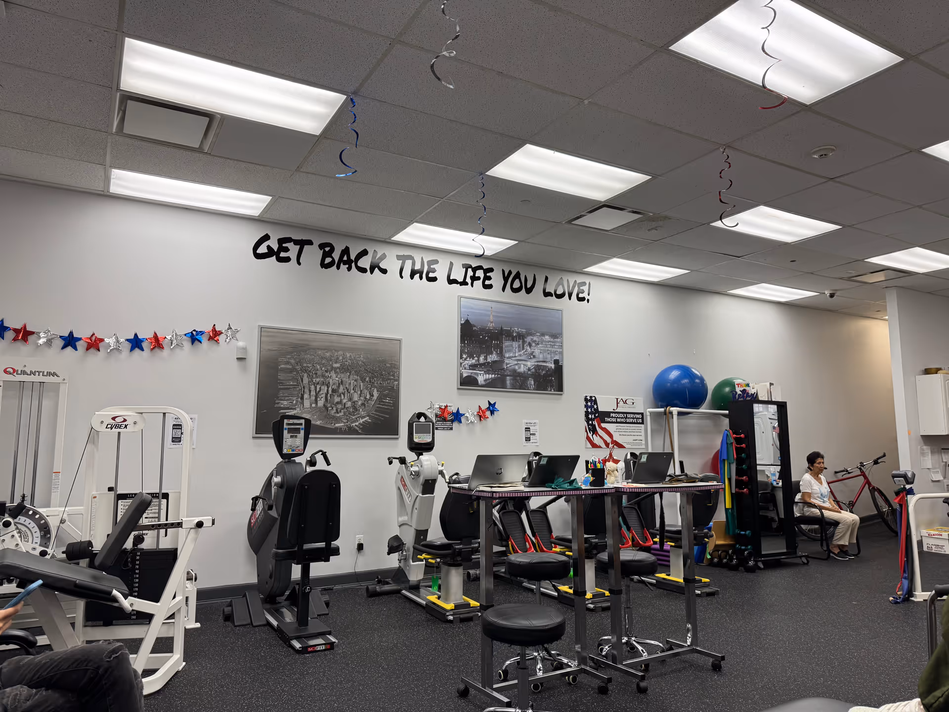 Interior at JAG Physical Therapy gym with equipment and a seated person by wall decor.