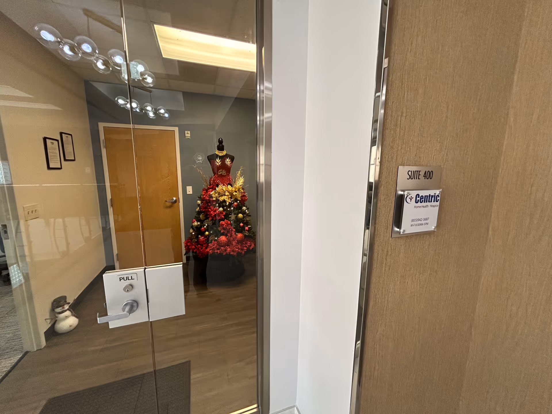 Glass entry doors to a facility lobby with a Christmas tree and holiday decorations.