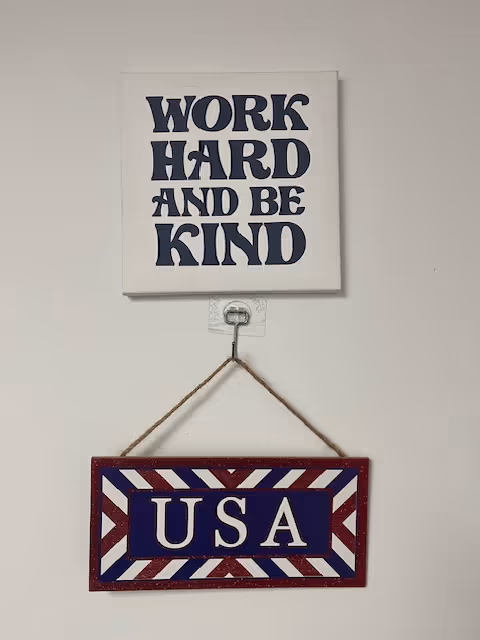 Interior wall with a framed WORK HARD AND BE KIND sign and a hanging USA plaque.