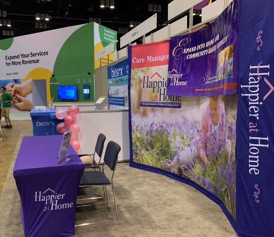 Exhibition booth for Happier at Home with purple banners, tables, chairs, and balloons.