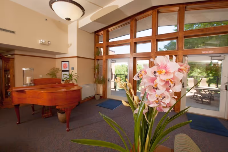 Wooden grand piano beside a vase of pink orchids in a spacious lobby.