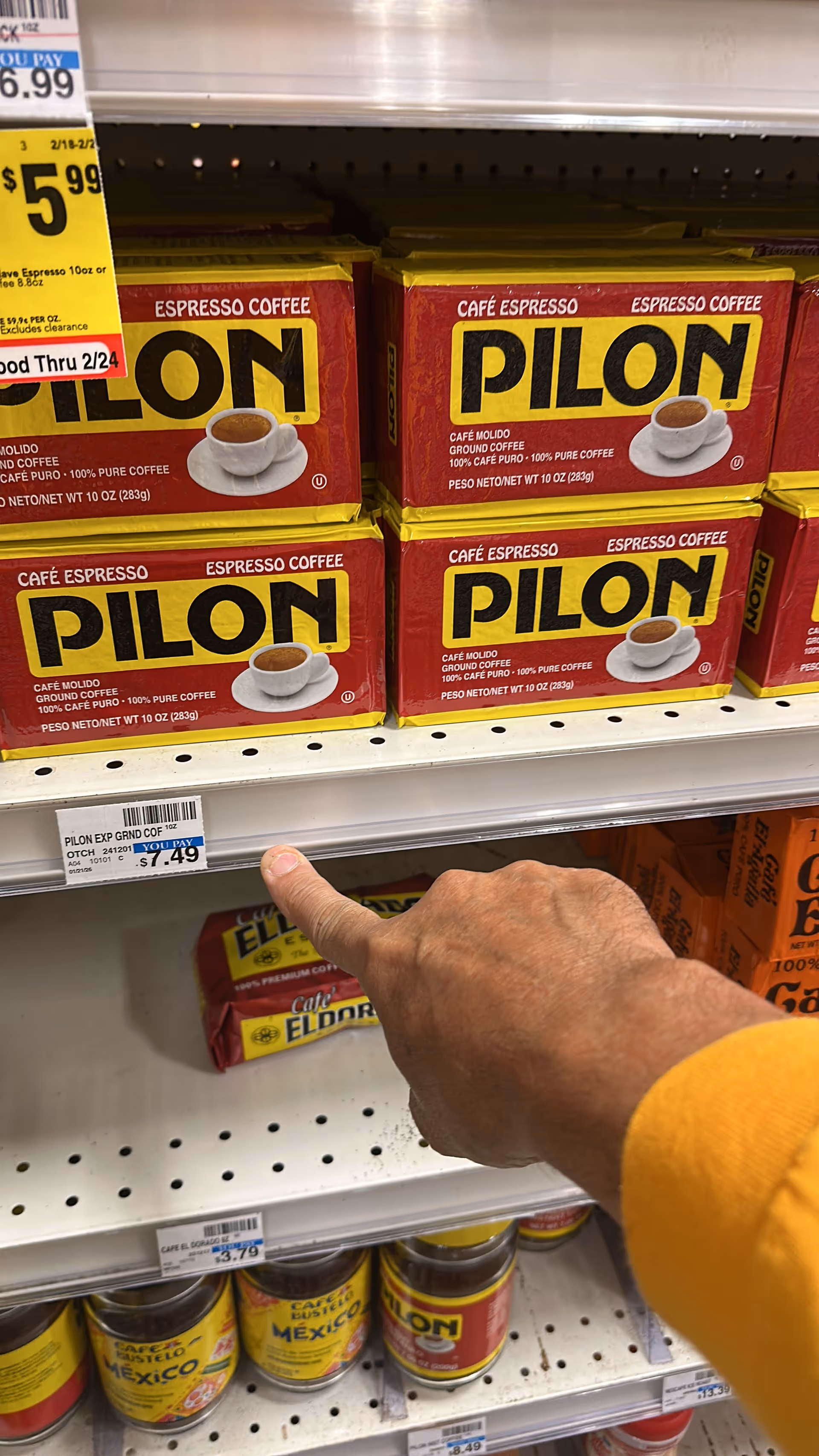A hand points at Pilon espresso coffee boxes on store shelves.