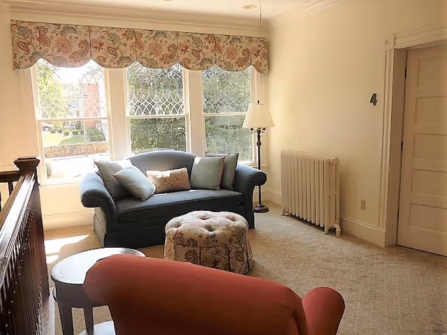 Cozy living room with blue sofa, red chair, ottoman, lamp, and large windows.