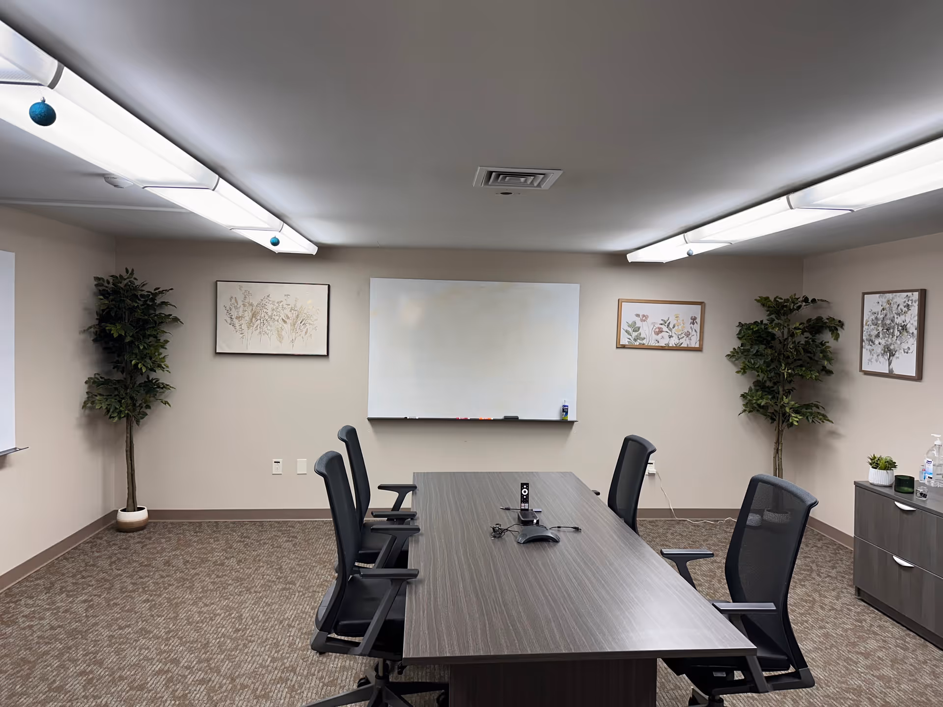 An empty conference room with a long table, chairs, whiteboard, and framed art.