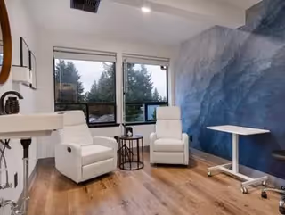 Two white recliners sit beside a small round table in a bright living room.