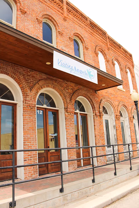 Brick building exterior with arched windows and a Visiting Angels sign.