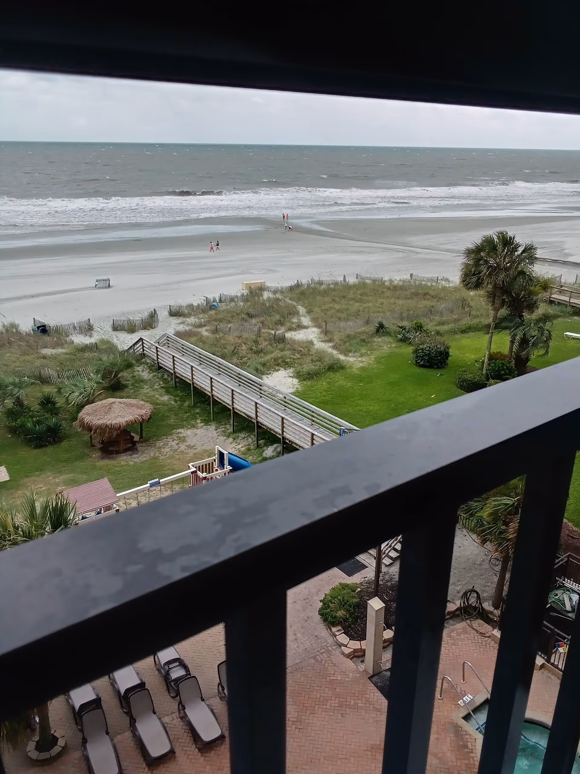 Balcony view of the beach, boardwalk, pool, and grassy lawn.