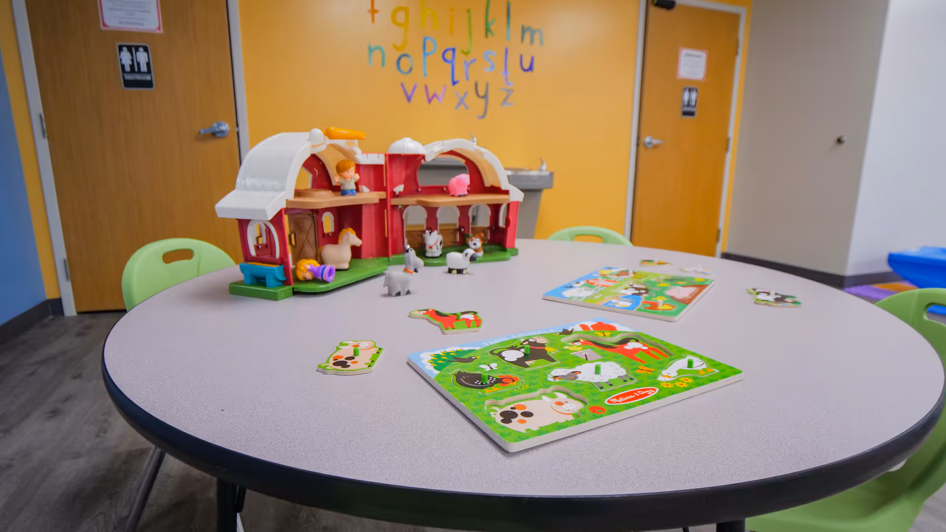 Round table with a toy playset and jigsaw puzzles in a bright ABA therapy playroom.