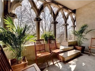 Arched outdoor terrace with wooden chairs, potted plants, and sunlight.