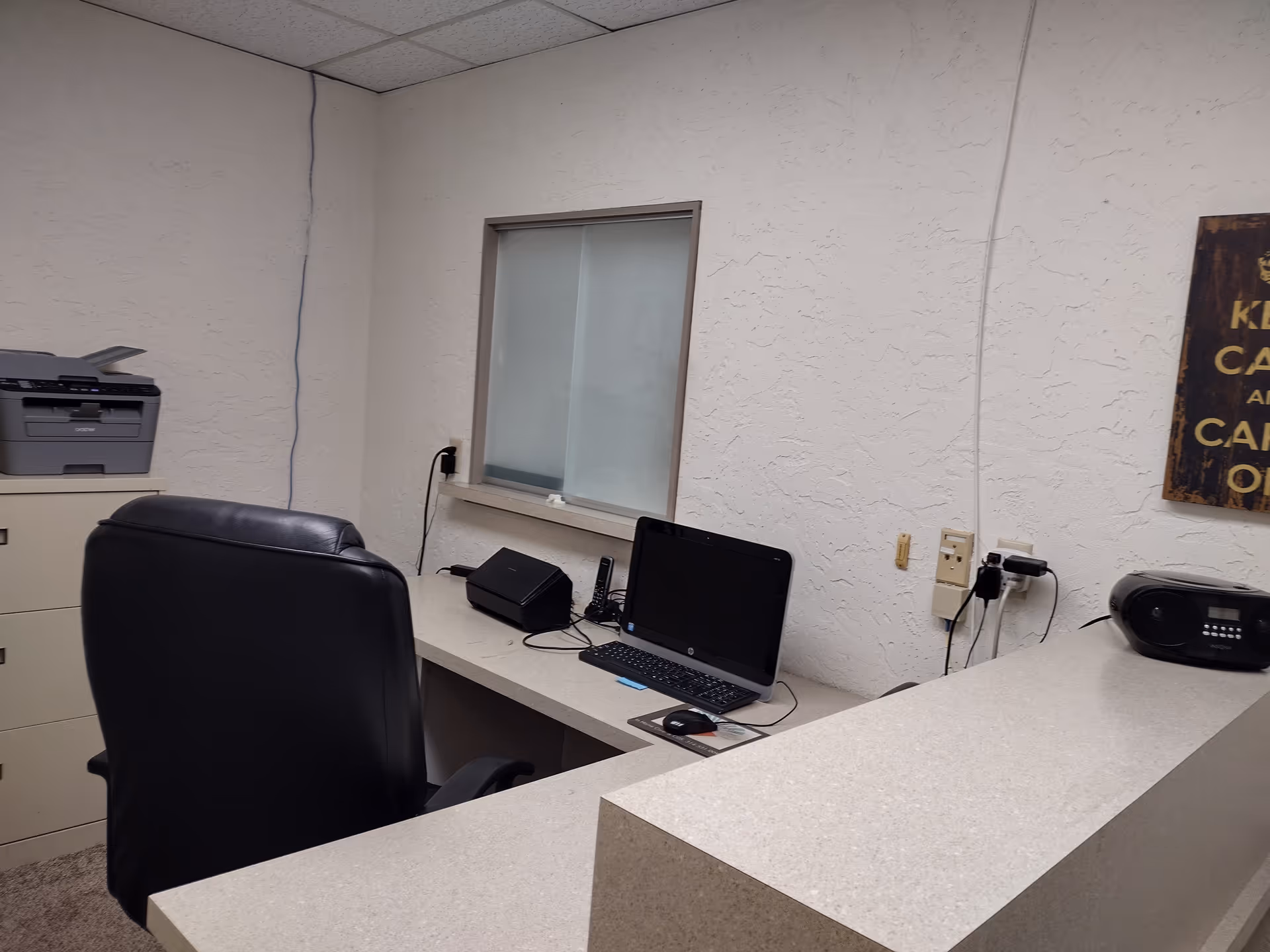 Office workstation with computer, printer, and reception desk in a small interior room.