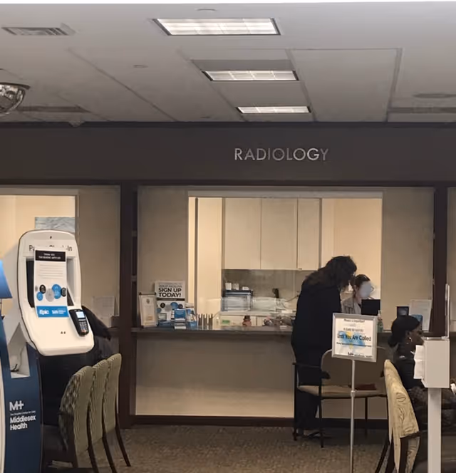Interior radiology reception area with sign, desks, and patients waiting.