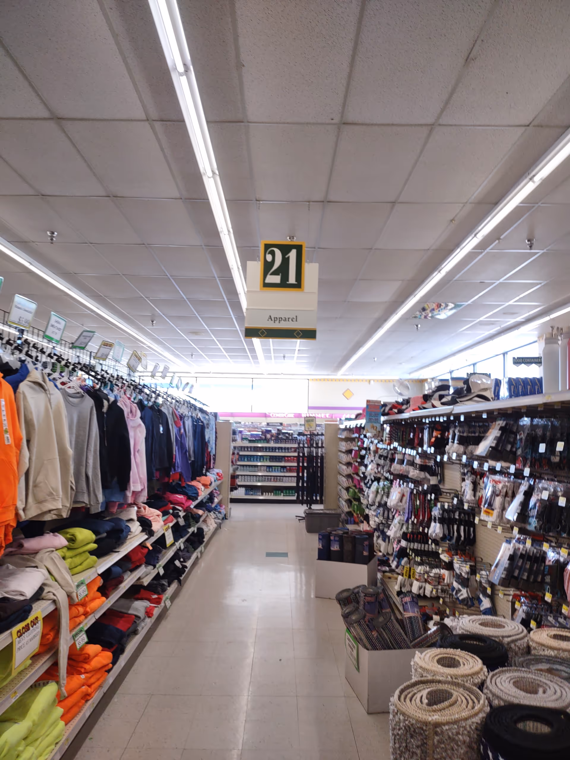 Long aisle inside Discount Drug Mart with clothing racks and shelves.