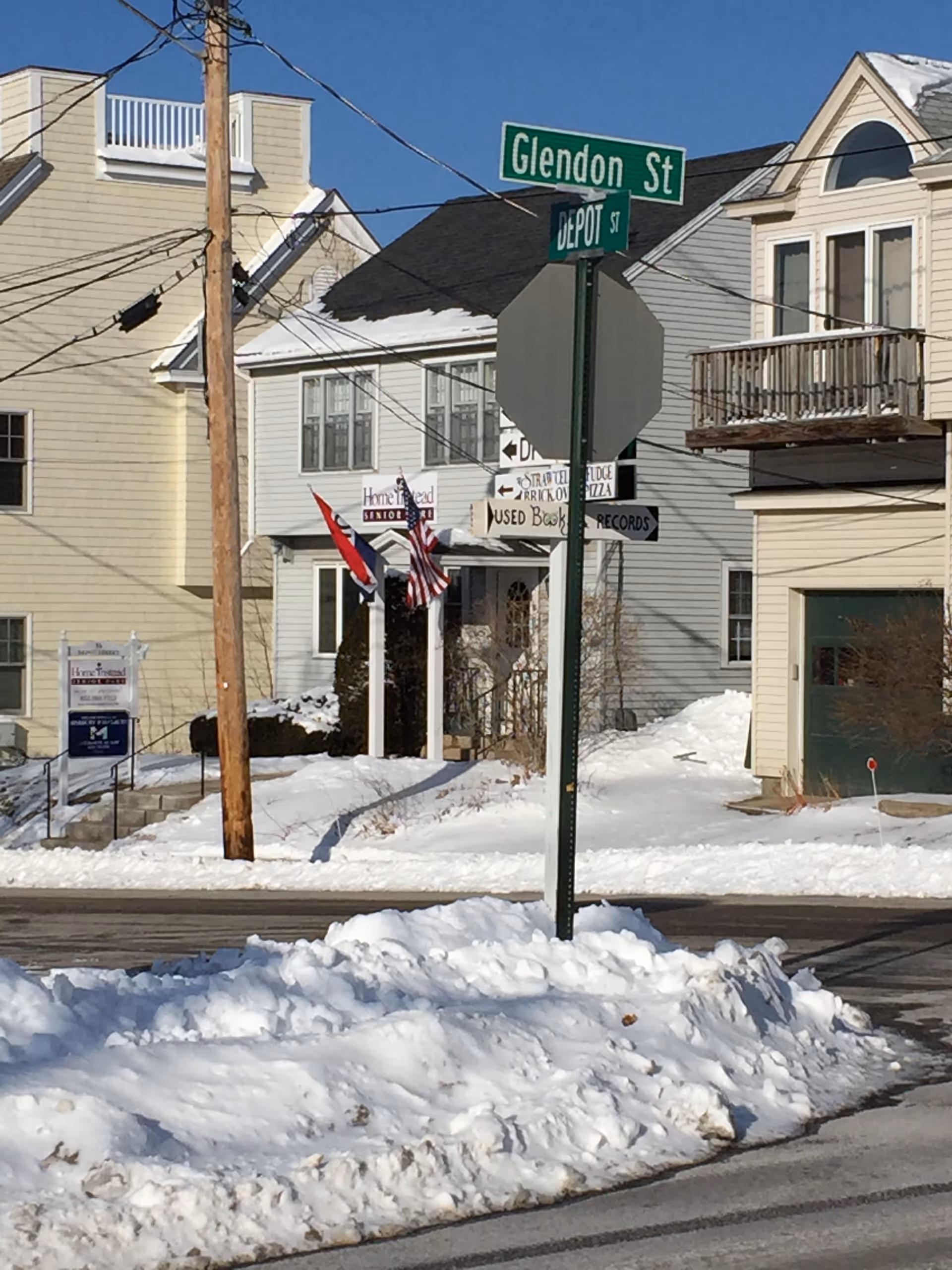 Snow-covered street corner with residential houses and street signs.