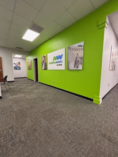 Bright green hallway with framed posters in a carpeted MobilityWorks facility.