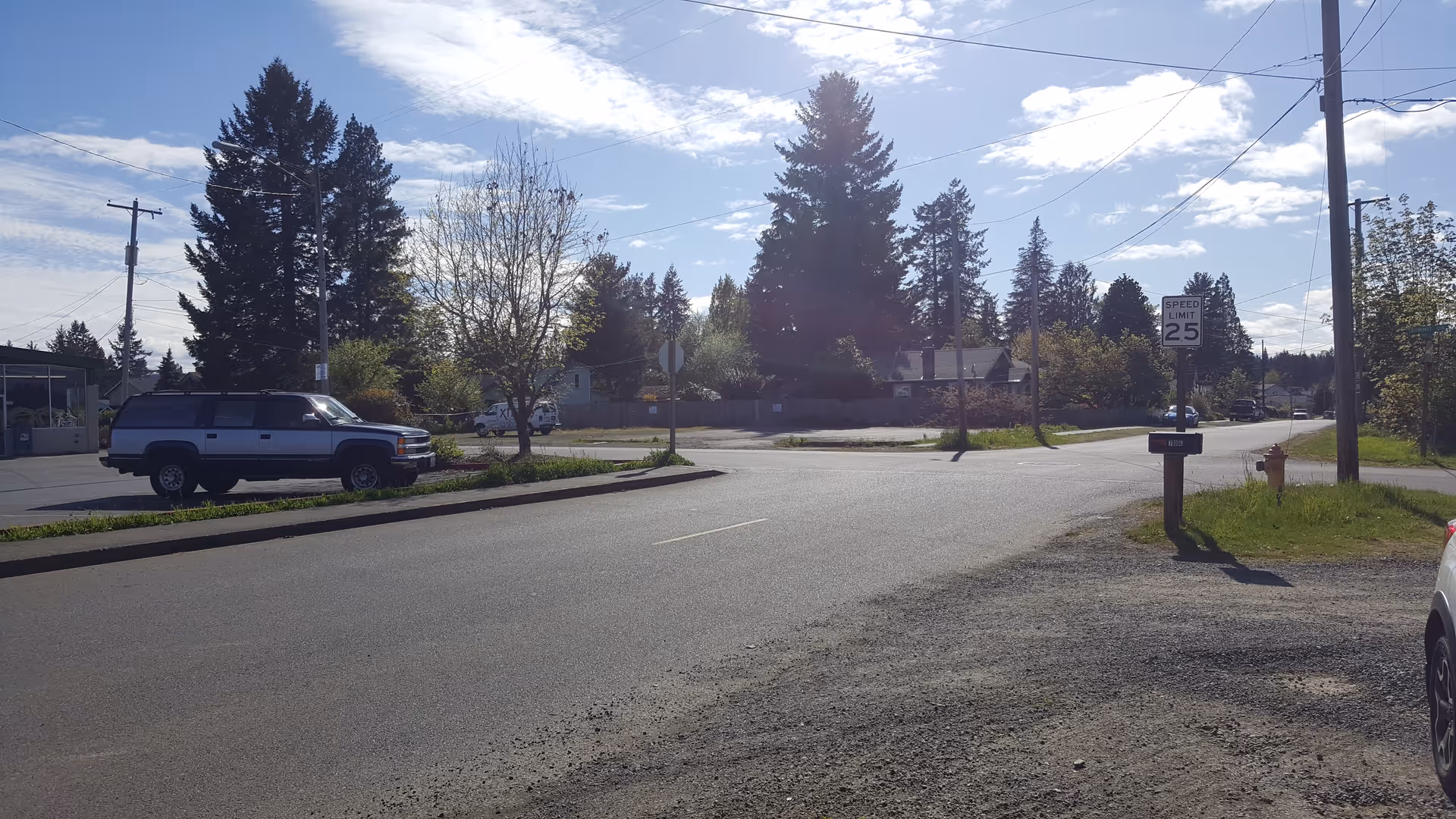 Quiet residential street at a suburban intersection with trees and parked vehicles.