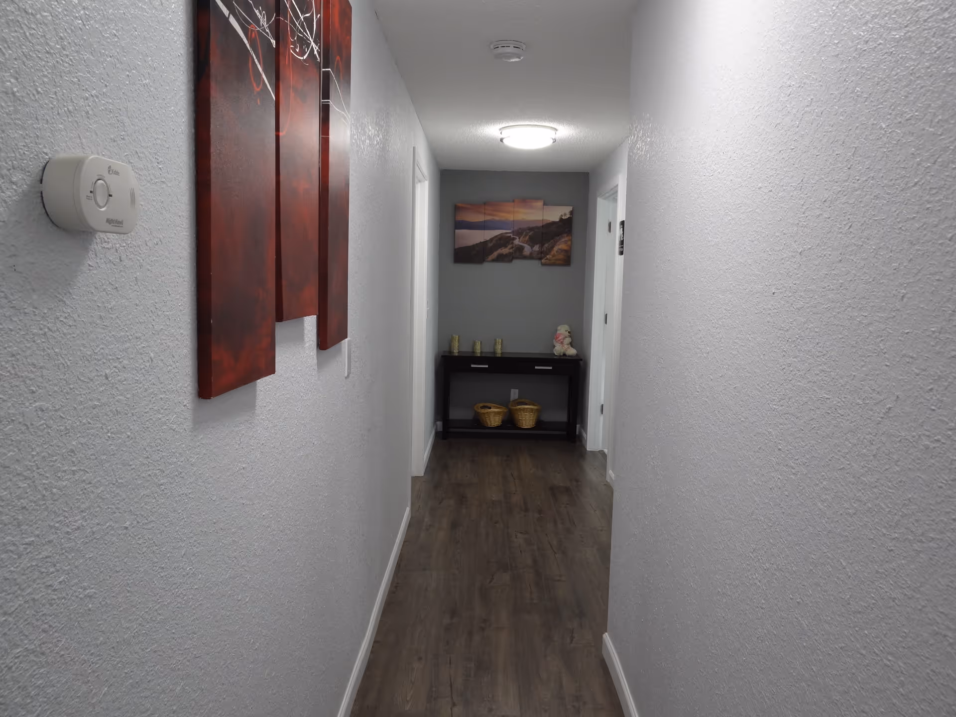 Narrow hallway inside a senior living facility with wall art, a console table, and baskets.