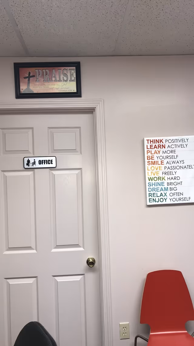 Interior hallway with an office door, praise artwork, and red chairs.