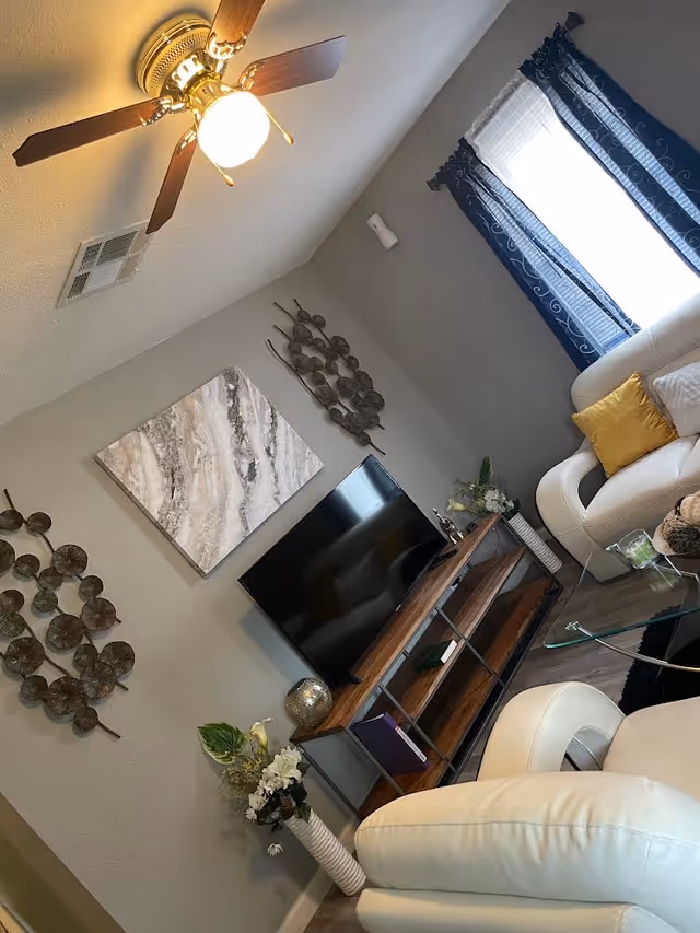 Living room in a senior facility with white leather chairs, TV, and decorative wall art.