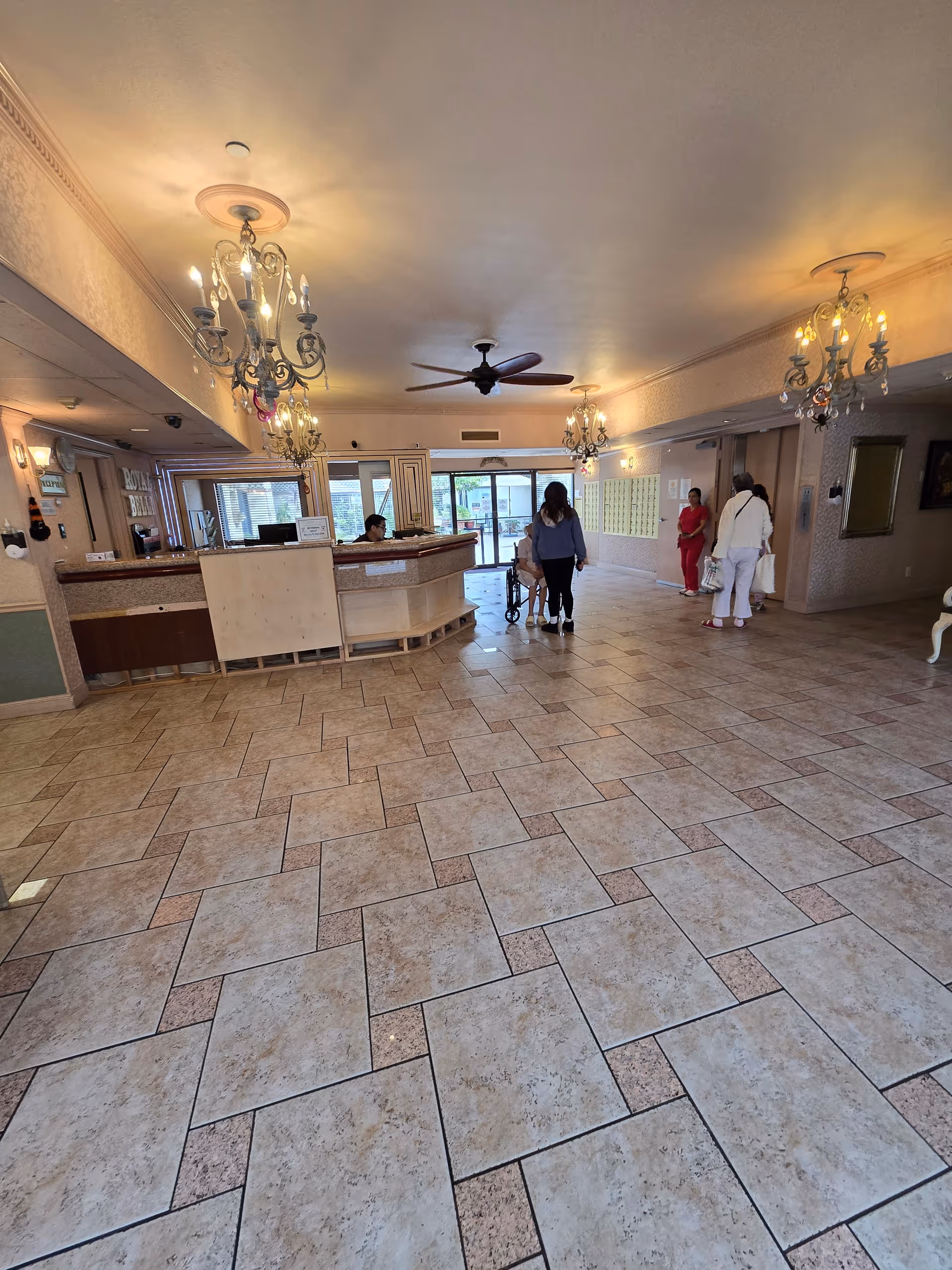 Spacious senior living facility lobby with a reception desk, chandeliers, and tiled floor.