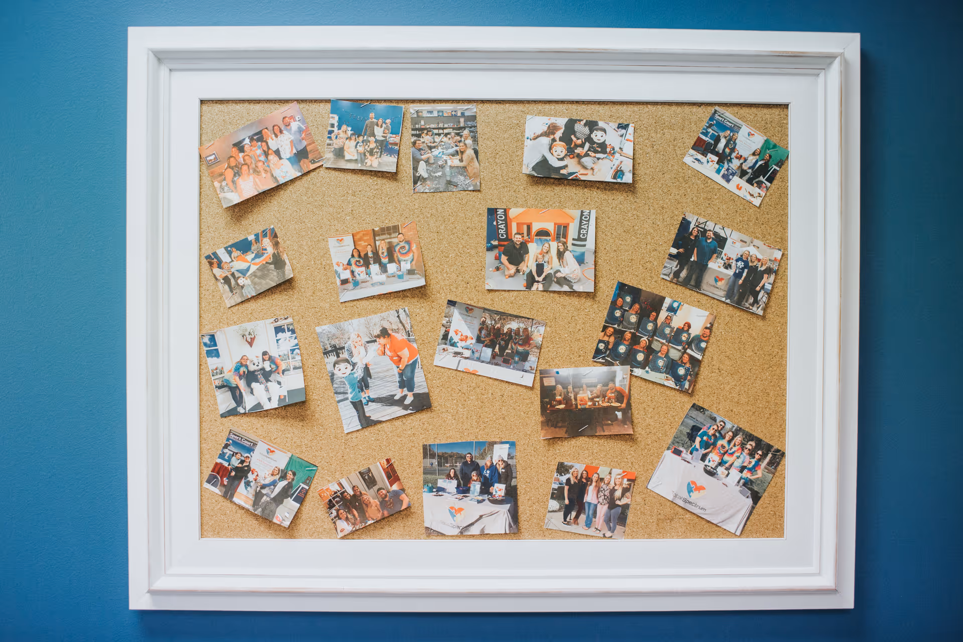 White-framed cork bulletin board displays numerous photos on a blue wall.