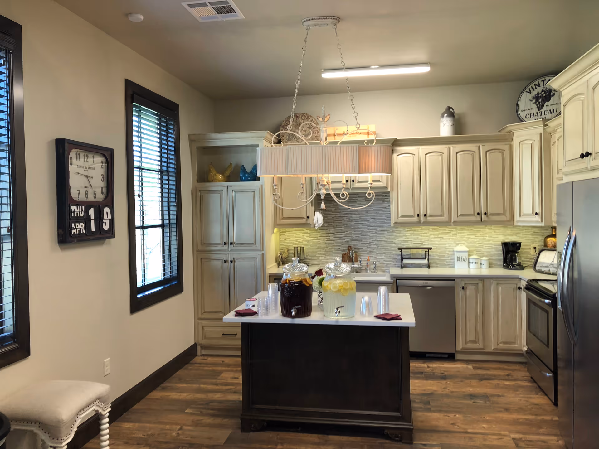 Bright kitchen with white cabinets, an island, a hanging chandelier, and beverages on the island.
