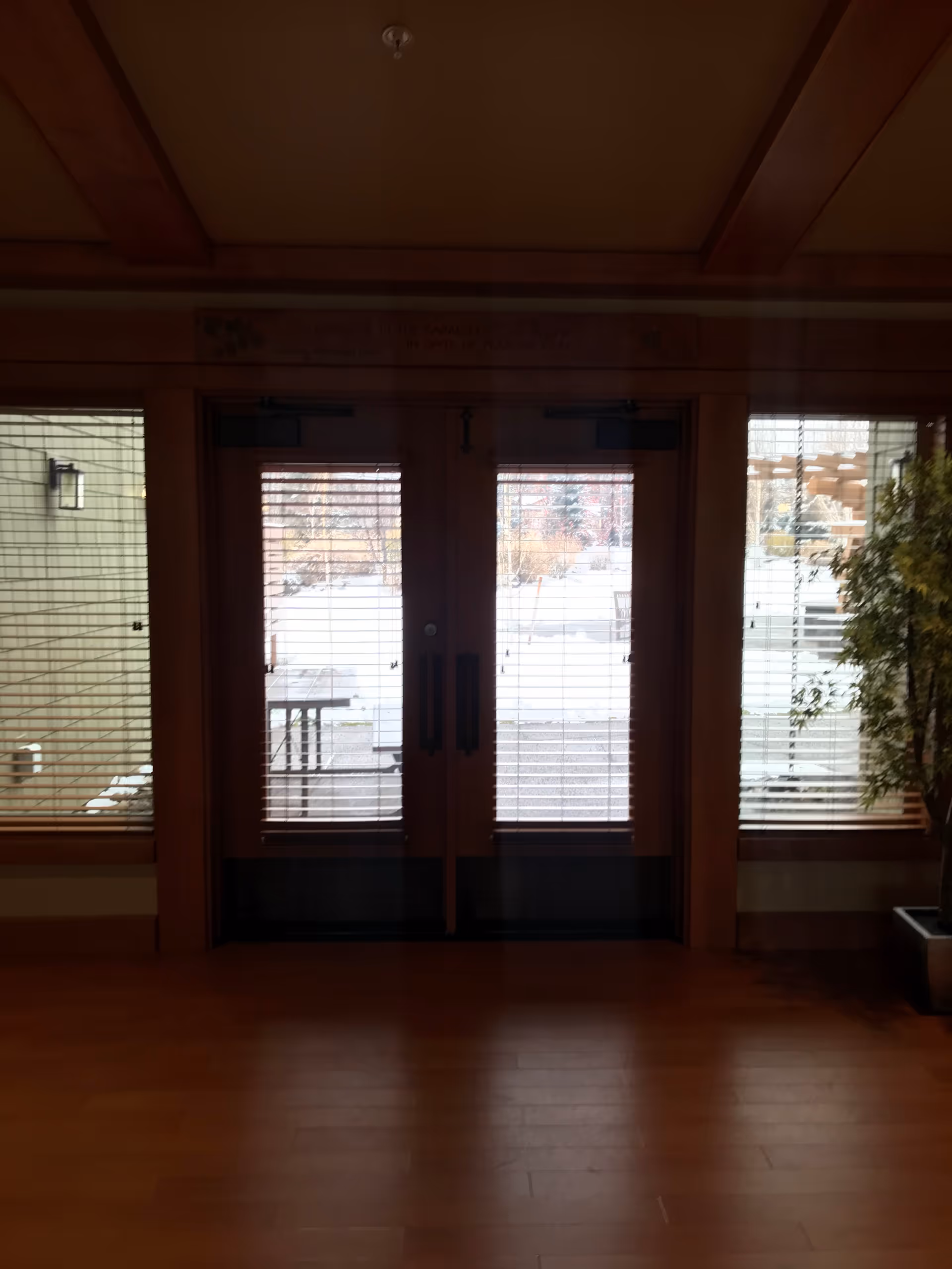 There are double glass doors with blinds in a wood-floored interior lobby.