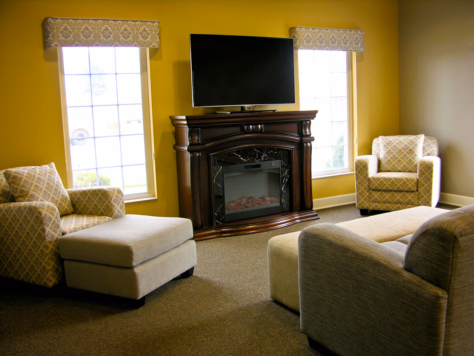 Cozy living room with a fireplace, TV, and armchairs by two windows.