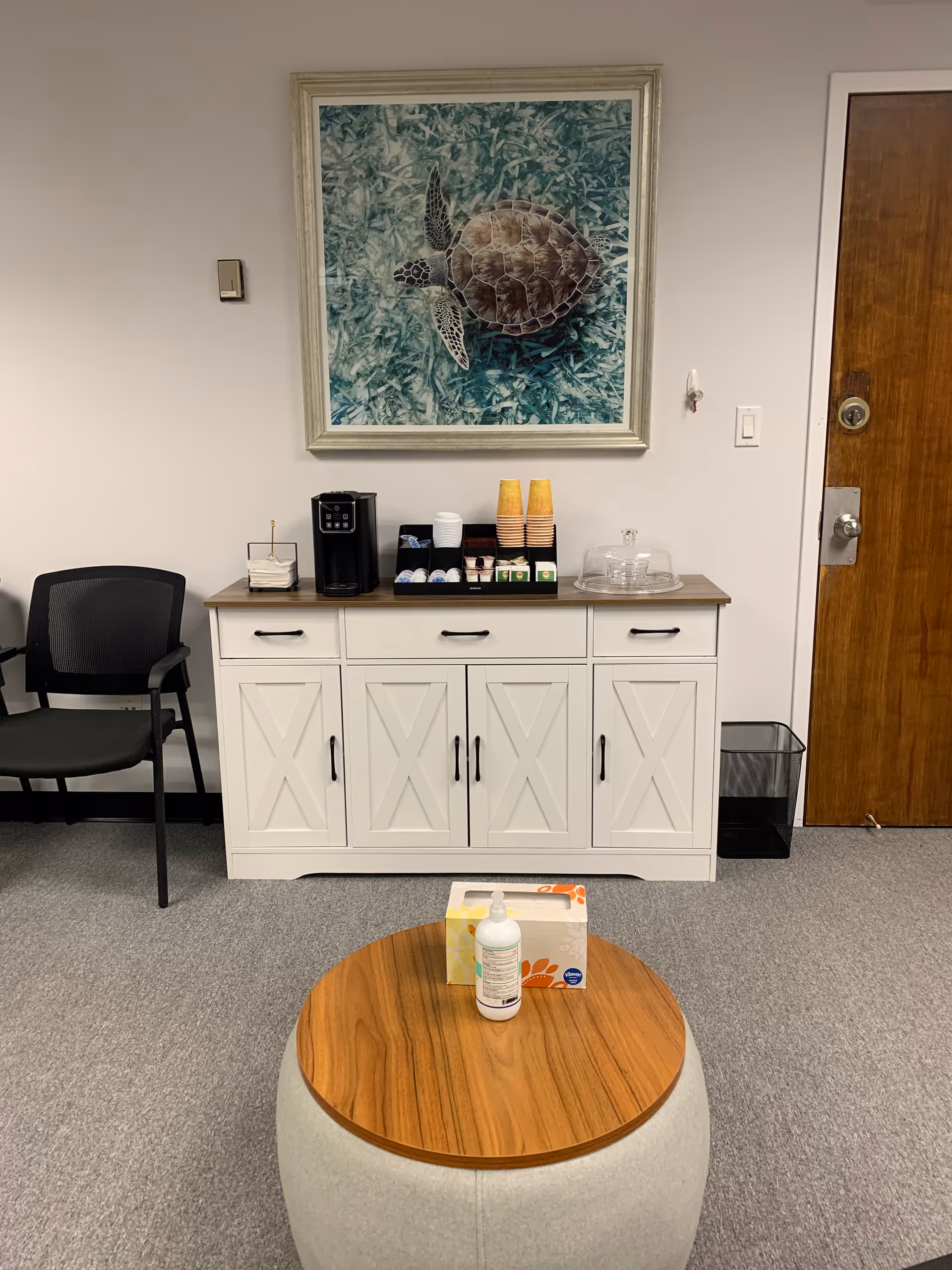 Coffee station and seating area against a wall with a turtle artwork.