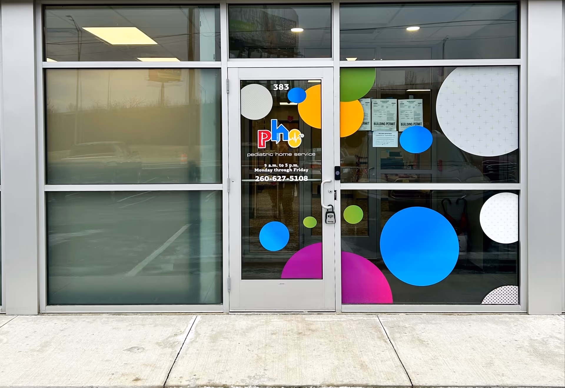 Glass storefront entrance with colorful circular decals and signage for Pediatric Home Service.