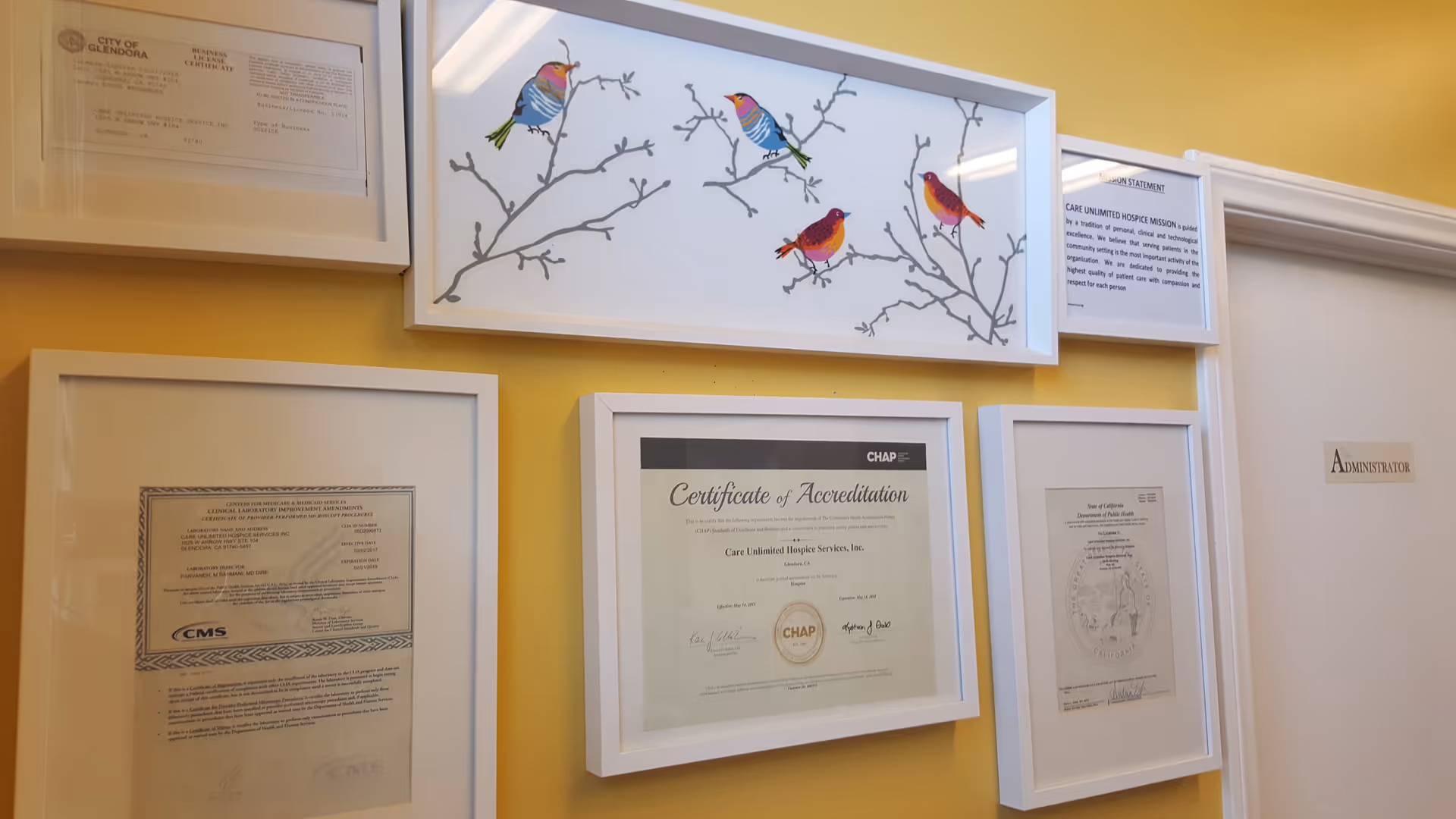 Yellow-walled interior hallway displaying framed certificates and bird artwork.