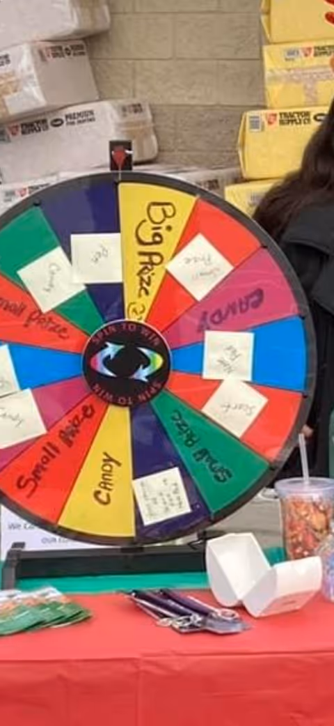 Colorful prize wheel on a table indoors with notes and boxed supplies nearby