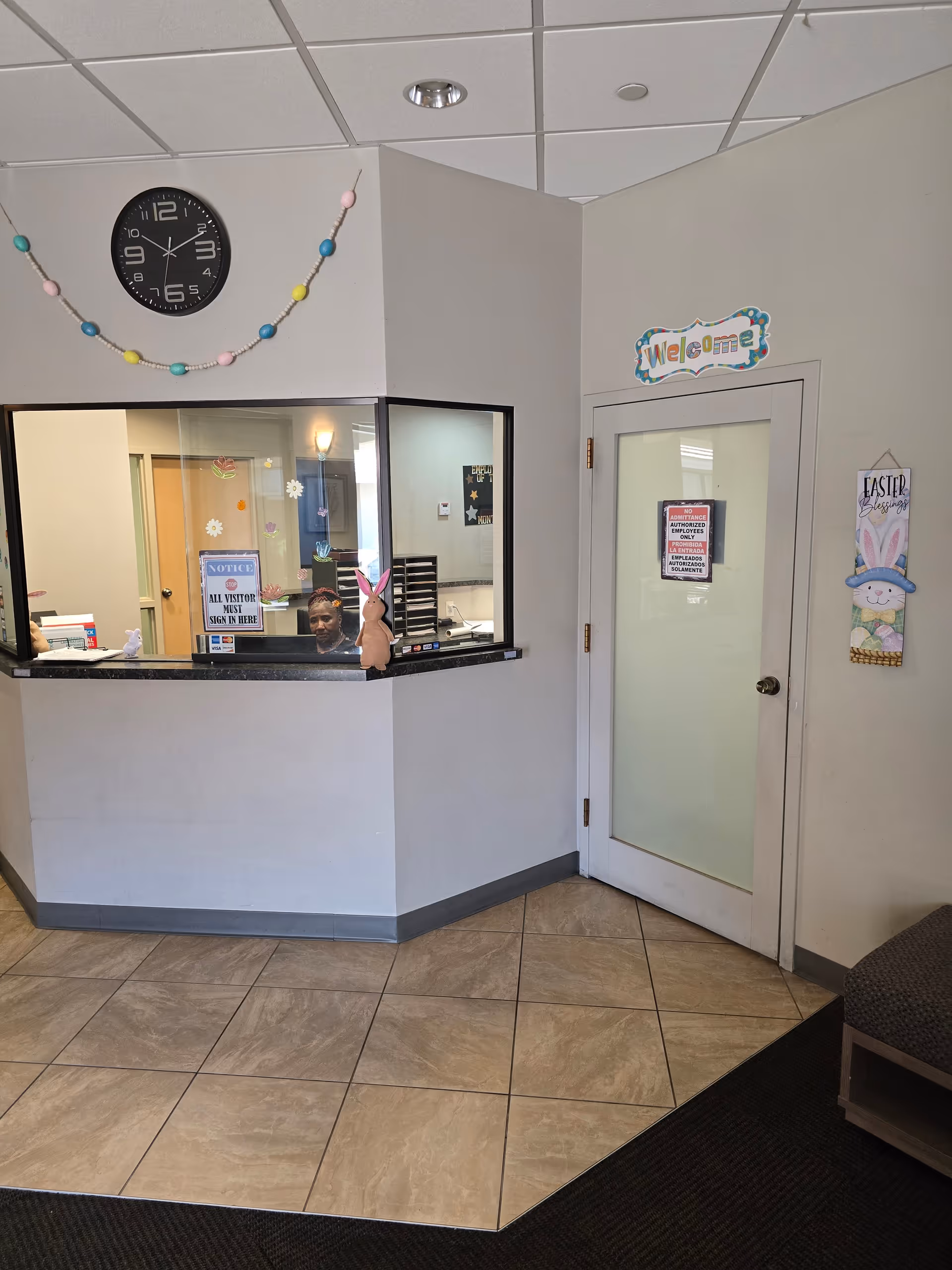 Reception area with a counter, clock, Easter decorations, and a staff member behind the window.