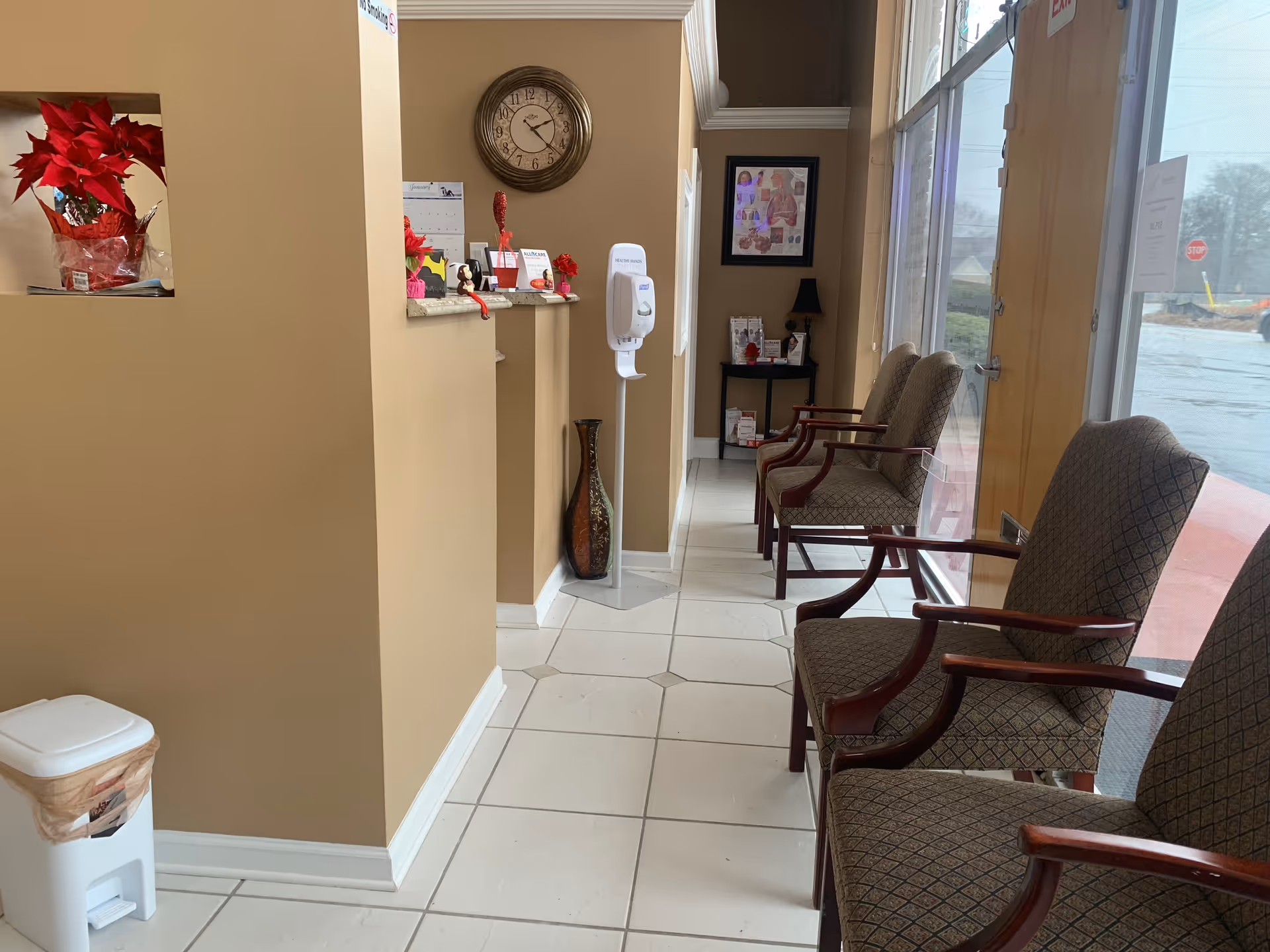 Beige-walled reception area with a row of chairs and large glass windows.