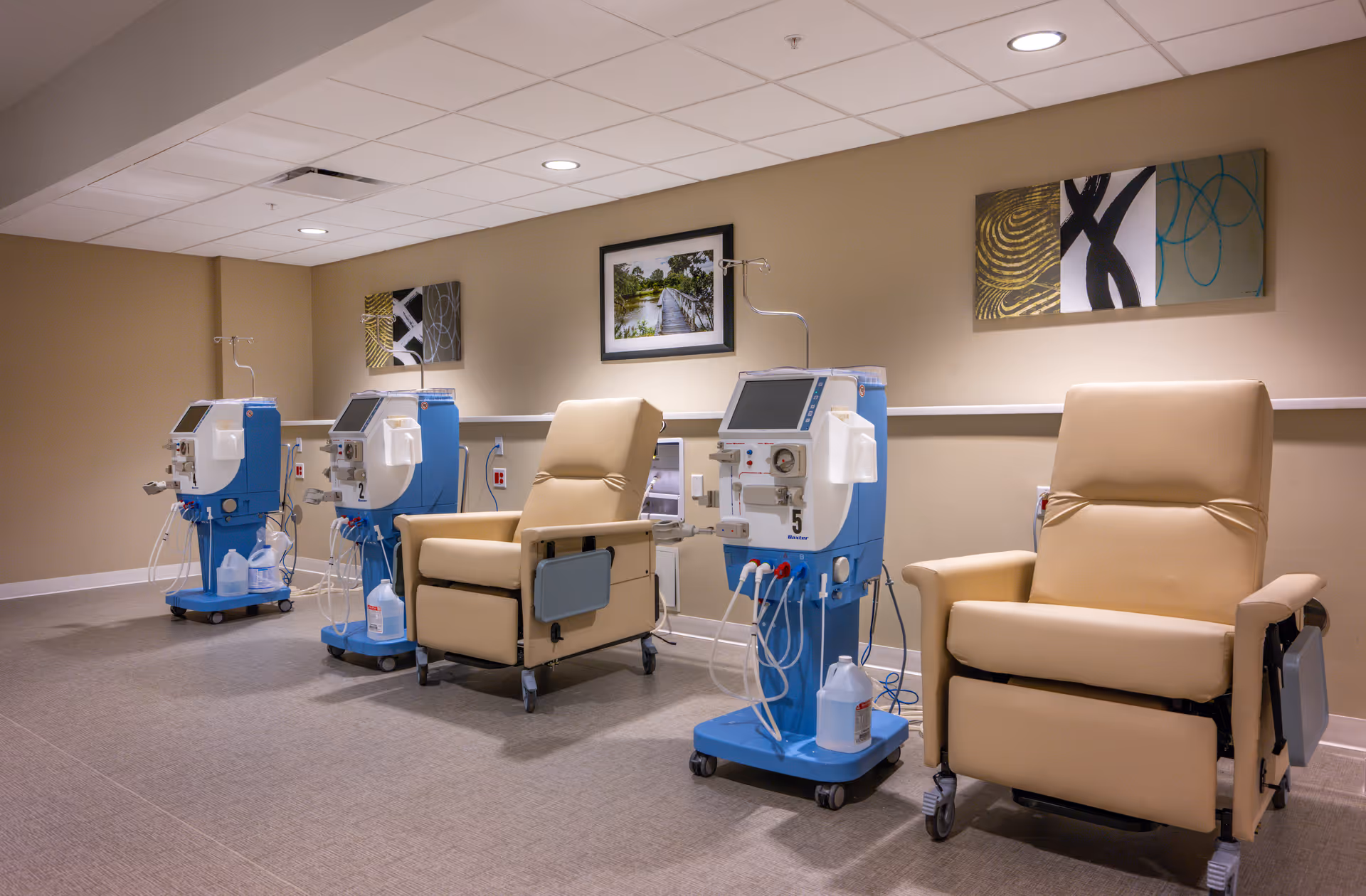 A medical treatment room with reclining chairs and multiple dialysis machines.