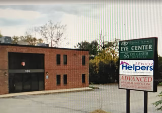 Brick building exterior with Senior Helpers and Eye Center signs near a parking lot.