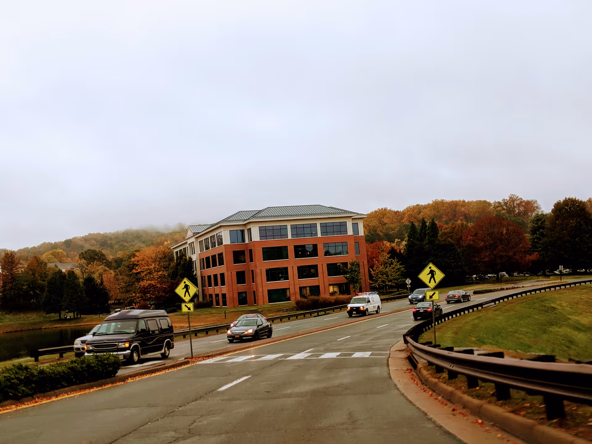 Exterior view of a brick, multi-story facility by a road with autumn trees.
