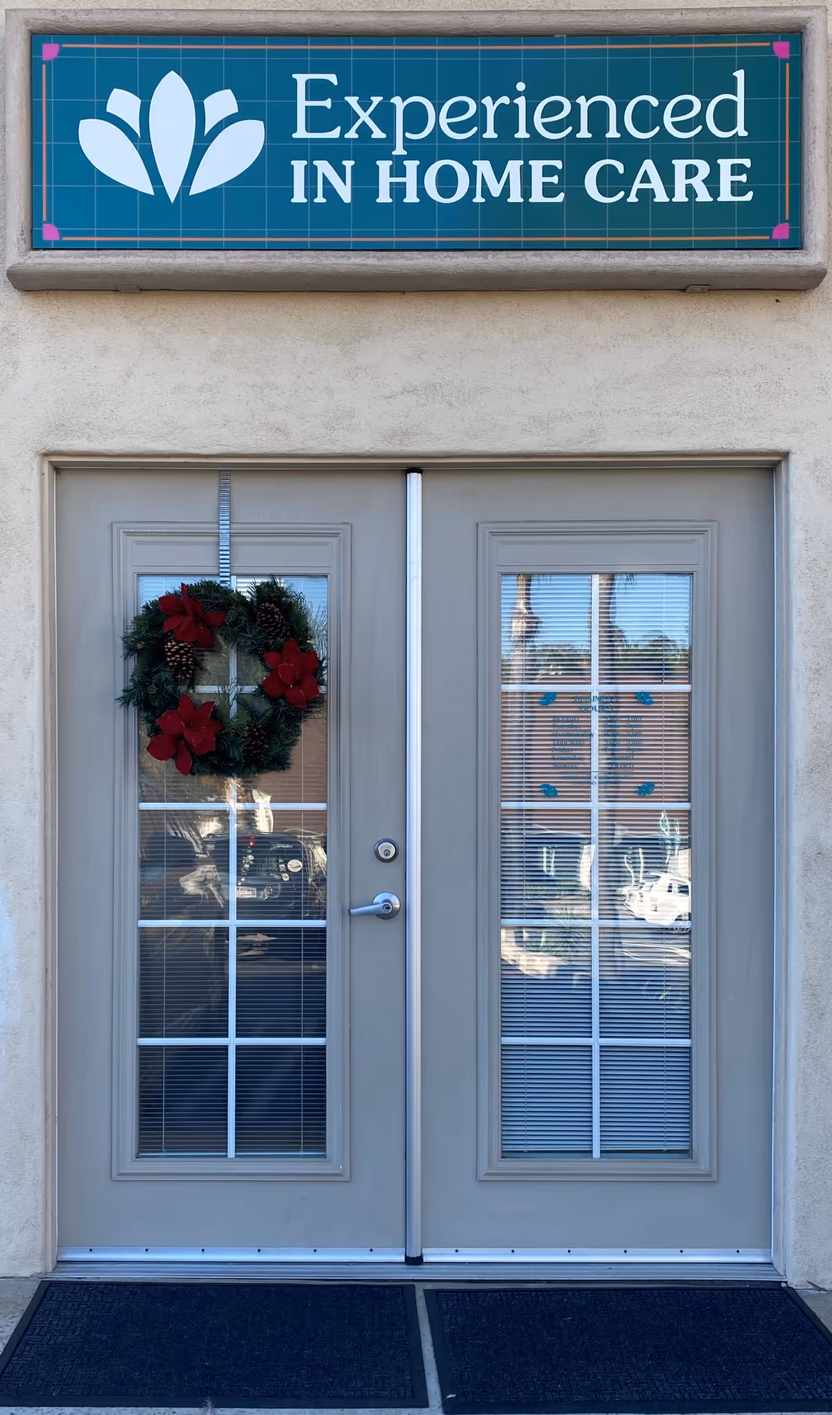 Exterior entrance with double doors, sign reading Experienced In Home Care, holiday wreath on left door.