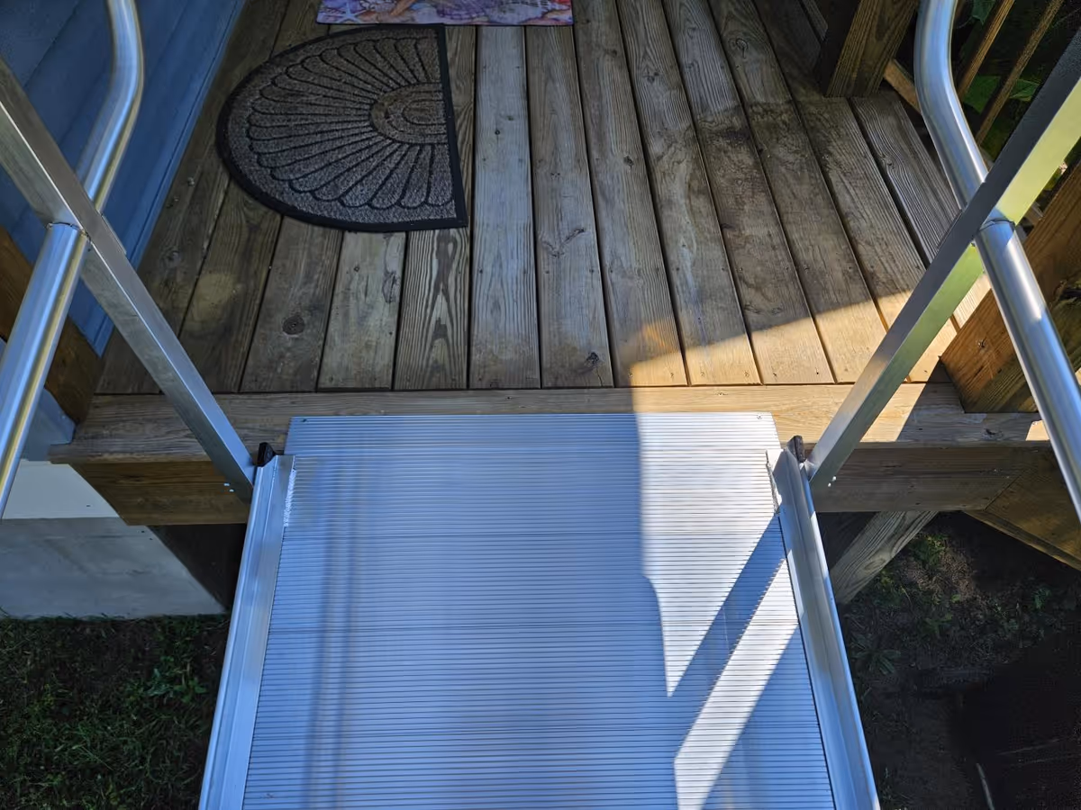 Exterior wooden deck with metal ramp and steps leading to a doorway.