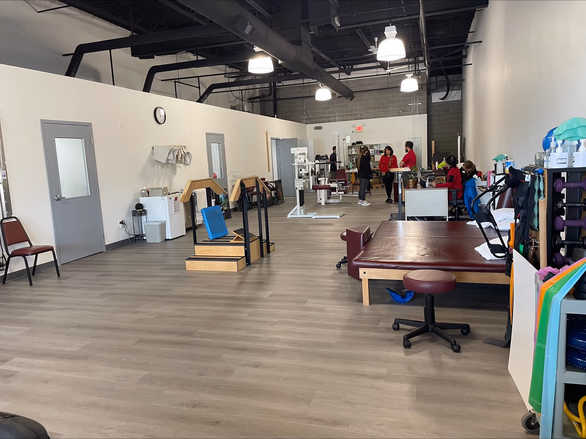 Wide view of a physical therapy gym with equipment, mats, and staff near back desks.