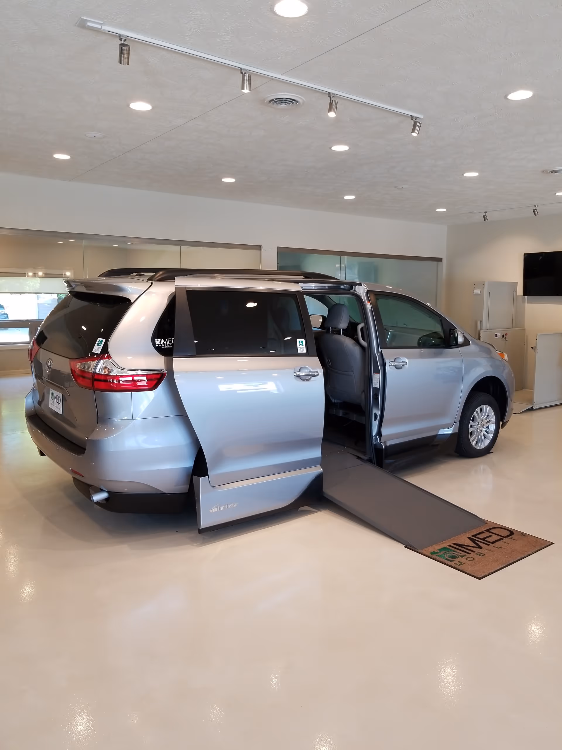 Inside a MobilityWorks showroom, a silver minivan with a deployed ramp sits ready.