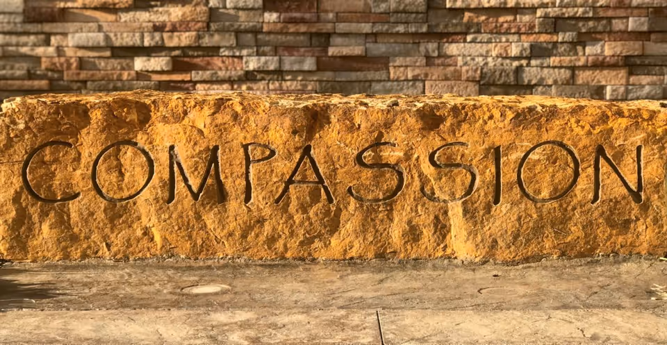 Close-up of a stone sign reading COMPASSION at a building entrance.