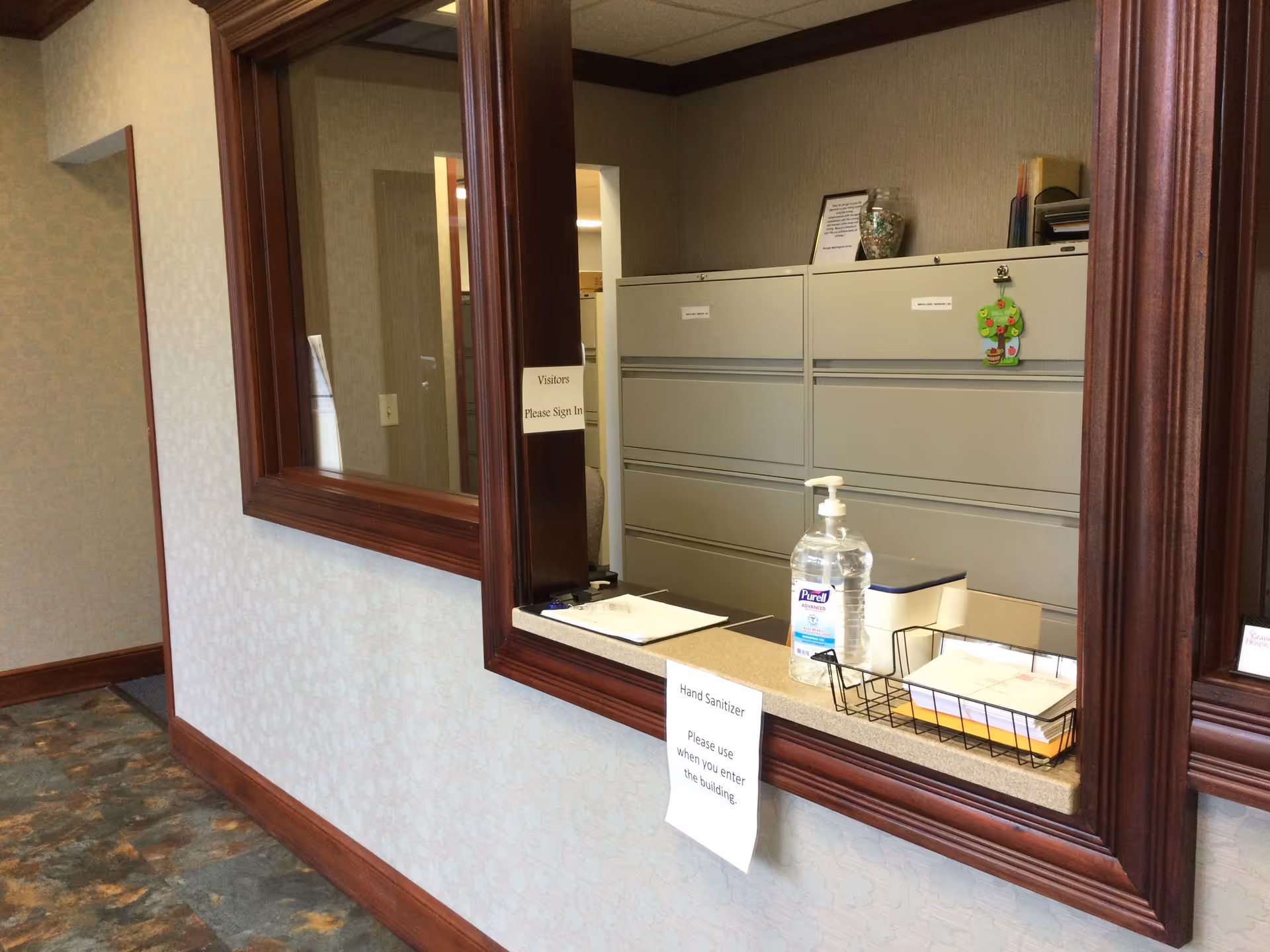 Interior reception area with counter, hand sanitizer, and a wall of gray filing cabinets.