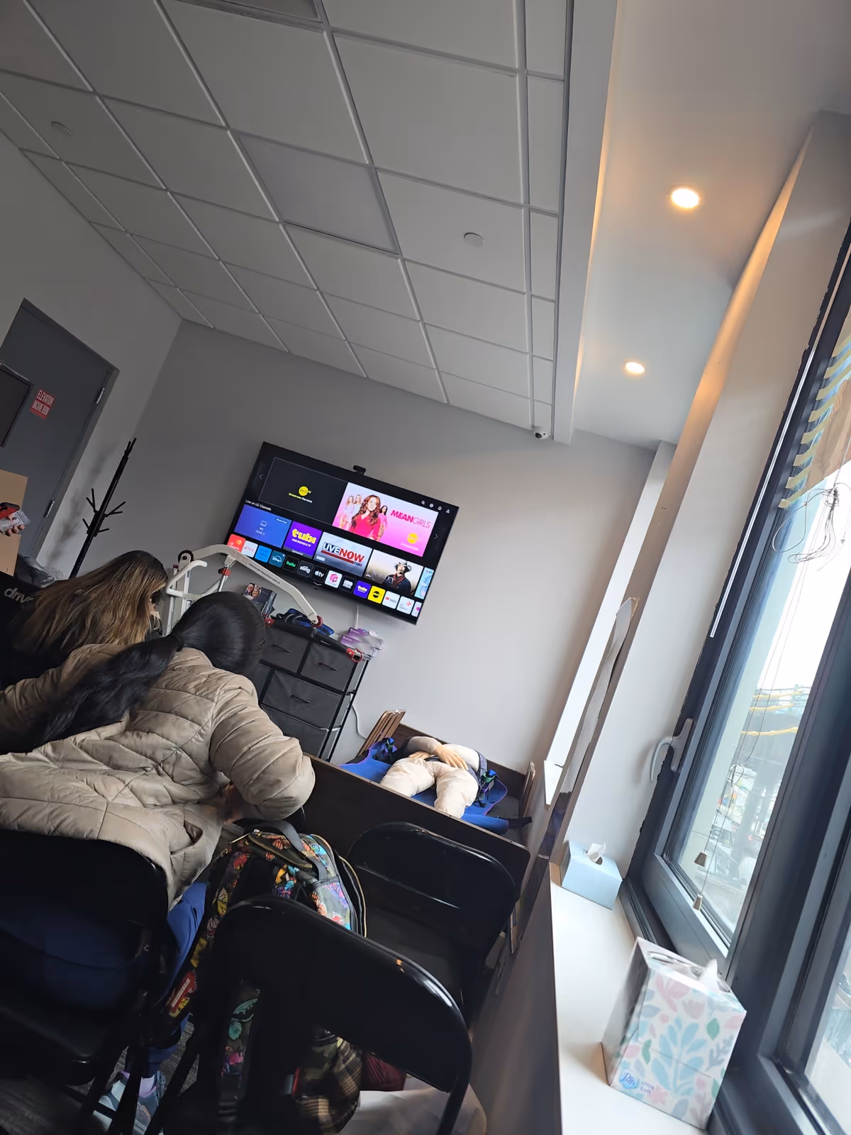People sit in a bright living room watching a wall-mounted TV.