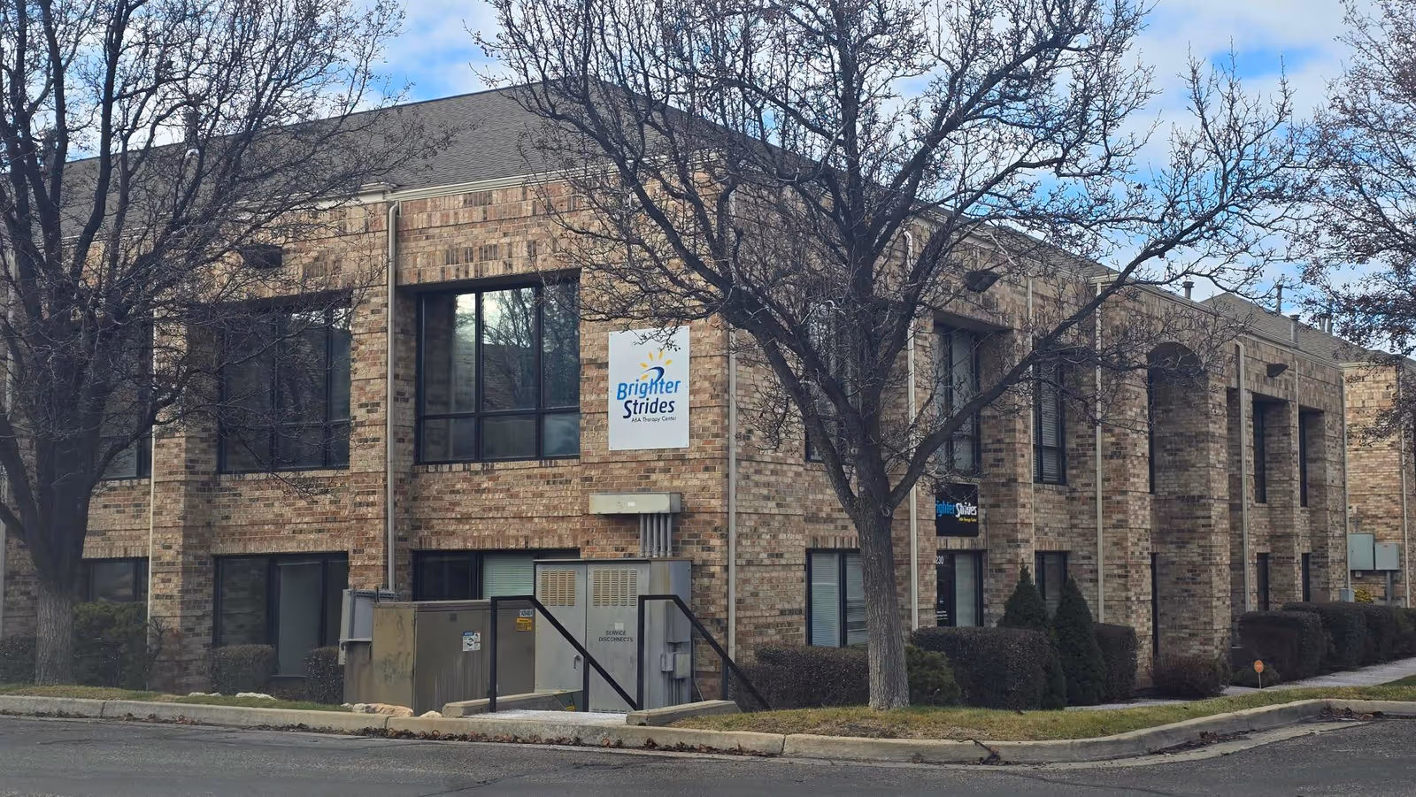 Exterior brick building with Brighter Strides ABA Therapy sign and leafless trees.