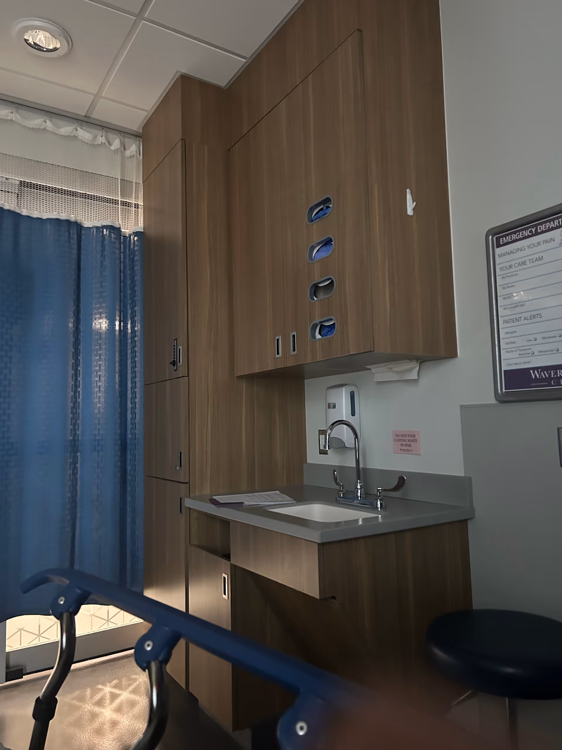 Wooden cabinets and a sink in a clinical room with blue privacy curtains.